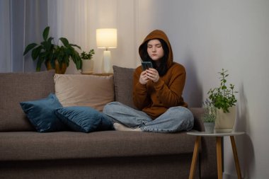 Akşamları kanepede akıllı telefonlu genç kız.