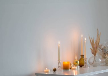 Beyaz odada yanan mumlarla Noel süsleri.