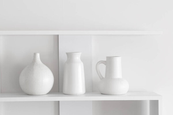 белые керамические вазы на деревянной полке на белой стене