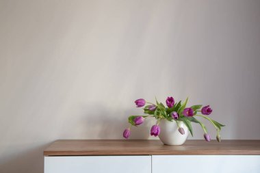 Beyaz seramik vazoda, ahşap rafta mor laleler.