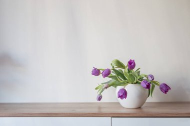 Beyaz seramik vazoda, ahşap rafta mor laleler.