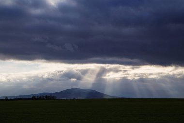 Dağları ve bulutlu gökyüzü olan koyu mavi bir manzara.