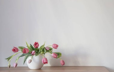 Beyaz seramik vazoda, ahşap rafta mor laleler.