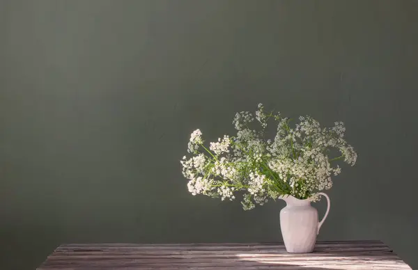 white wild flowers in jug on background green wall