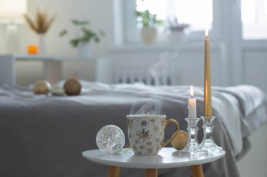 Beyaz yatak odasındaki küçük masada noel topları olan bir fincan kahve.