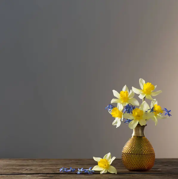 黄色のナルシシズムと青い雪が暗い背景の木のテーブルの上に花瓶に落ちる — ストック写真