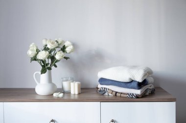 Modern şifoniyerdeki sürahide örülmüş giysiler ve beyaz güller