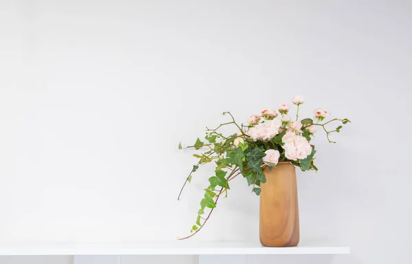 pink roses with ivy in vase on shelf on background white wall