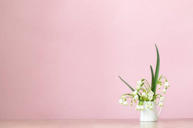 Pembe arka planda sürahi içinde beyaz bahar çiçekleri