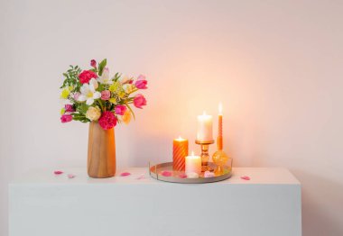 Vazodaki çiçekler ve arkadaki duvardaki rafta yanan mumlar.