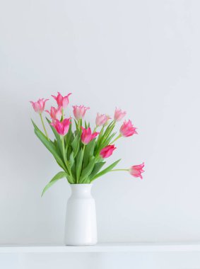 Beyaz arkaplanda beyaz vazoda pembe laleler