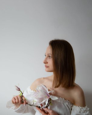 Gri arka planda bahar çiçekleri olan beyaz elbiseli zarif bir kadın.