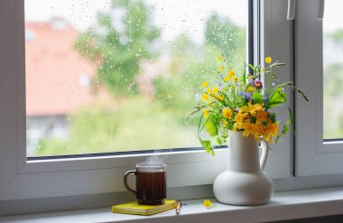 Beyaz sürahide yaz çiçekleri Pencere kenarında bir fincan çayla