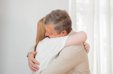 Baba ve kızı beyaz duvara sarılıyorlar.