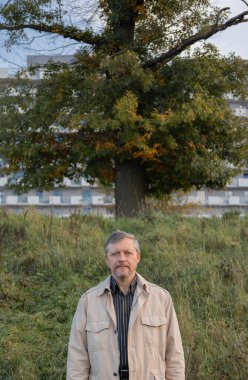 Arka plandaki ağaç ve modern evdeki orta yaşlı adamın portresi.