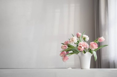 Arka plandaki beyaz duvarda beyaz seramik vazoda pembe bahar çiçekleri