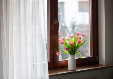 Pencere kenarındaki vazoda pembe laleler