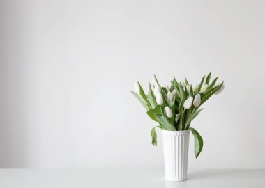 Beyaz vazodaki beyaz laleler arka plan duvarında