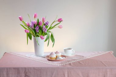 Bir fincan çay ve açık renkli bahar çiçekli kekler.