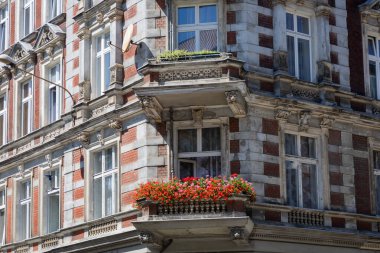 Çiçek açan pelargonyumları olan eski bir binada balkon.