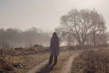 Bej renkli yağmurluklu kız güneşli bir günde yürüyor.