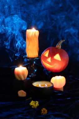 Koyu mavi arka planda yanan mumlarla Cadılar Bayramı kabağı