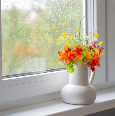 Pencere kenarında beyaz sürahi içinde yaz çiçekleri