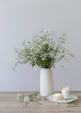 Yanan mumlar ve seramik vazodaki kır çiçekleriyle dolu ahşap bir masa.