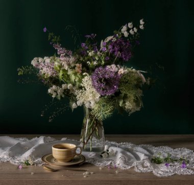 Cam vazoda yabani çiçekler ve yeşil arka planda seramik bardak.