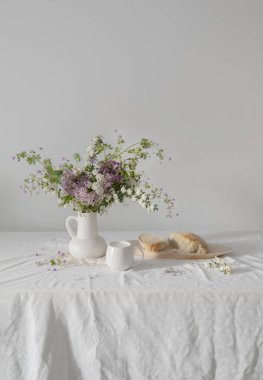 Seramik sürahide çiçekler, bir fincan süt ve ekmek