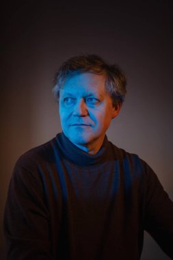 Siyah arka planda mavi ve kırmızı ışıklı orta yaşlı bir adamın portresi.