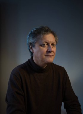 Karanlık arka planda gülümseyen orta yaşlı bir adamın portresi.