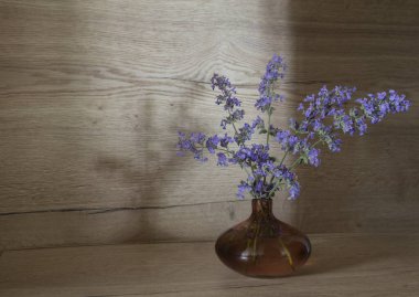 Ahşap arka planda cam vazoda mavi çiçekler.