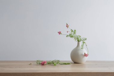 Yuvarlak seramik vazoda, açık ahşap masada pembe yabani çiçekler.