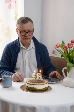 Doğum günü pastasında yanan mumlara bakan bir adam mutfakta tek başına.