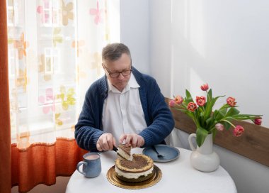 Yaşlı bir adam mutfağında pasta kesiyor.