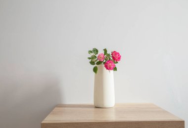 Seramik vazoda pembe güller Tahta masada beyaz iç kısımda