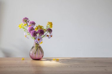 mor ve sarı çiçekler cam vazoda modern vazoda ahşap masada güneş ışığında