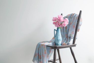 Pembe güller mavi sürahiyle arka planda eski ahşap sandalye beyaz duvar