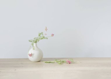 Yuvarlak seramik vazoda, açık ahşap masada pembe yabani çiçekler.