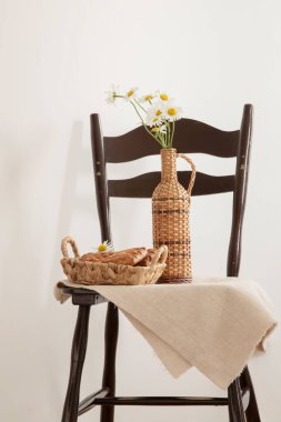 Eski bir şişede papatyalar ve eski bir sandalyede bir sepette pişmiş yiyecekler.