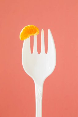 Pembe arka planda büyük beyaz bir çatal üzerinde küçük bir dilim mandalina.