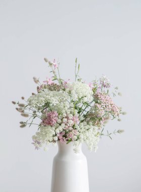 Beyaz vazoda beyaz ve pembe çiçekler. Arka planda beyaz duvar.