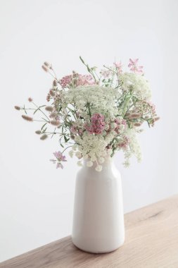 Beyaz vazoda beyaz ve pembe çiçekler. Arka planda beyaz duvar.