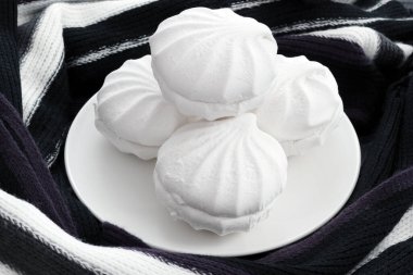 White zephyr marshmallow on plate with warm scarf around. Cozy sweet food. Airy and tender soft cakes.