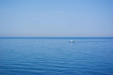 Küçük yalnız teknesi olan deniz pelerini. Mavi gökyüzü ile su yüzeyi.