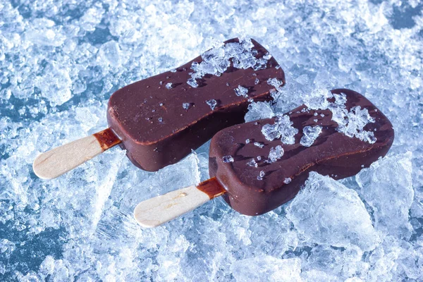 The chocolate coated ice cream bars on wooden stick on the chopped ice crystals.