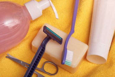 Kişisel temizlik seti sarı havlu arka planında. Günlük bakım için şampuan, makas, jilet, sabun ve diş fırçası..