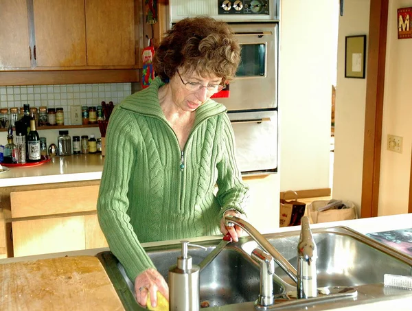 屋内キッチンで成熟した女性のシニアワーキングとクリーニングカウンター — ストック写真