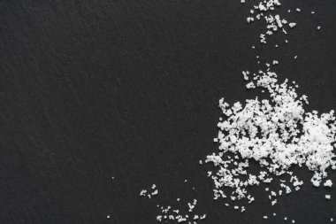 Sprinkled organic sea white salt on a black slate stone background. Concept of cooking natural healthy food. Copy space. 